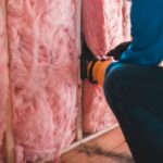 Crop unrecognizable worker in gloves sitting on haunches and insulating with pink stone wool - Photo by Erik Mclean on Pexels