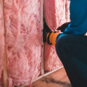 Crop unrecognizable worker in gloves sitting on haunches and insulating with pink stone wool - Photo by Erik Mclean on Pexels