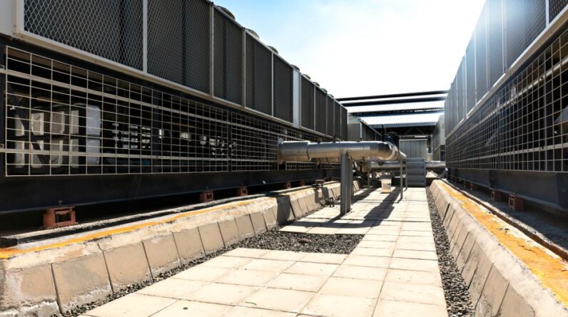 View of a large industrial cooling system with metal pipes and grids outdoors under bright daylight. - Photo by Tayssir Kadamany on Pexels